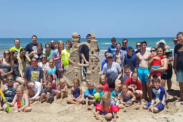 A group of 50 people of all ages after a Family Reunion Luxury VIP day on south padre island surrounding their amazing Twin-towered sandcastle which weighed 3000lbs and was 6ft high on the beach at south padre island Texas