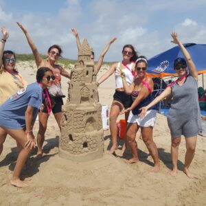 A group of 6 ladies celebrate building a big 6ft Sandcastle on the beach in South Padre Island during a reunion lesson with Andy Hancock which is a unique experience on the beach